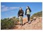 Twee mensen wandelen in outdoorjassen, T-shirts en broeken op een rotsachtig pad.