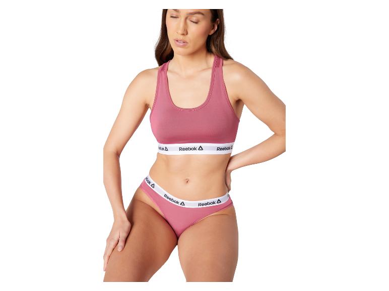 Vrouw in roze sportbeha en slip met Reebok-logo.