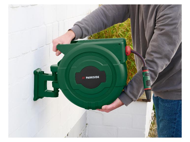 Man monteert een groene tuinslanghaspel aan een witte muur.