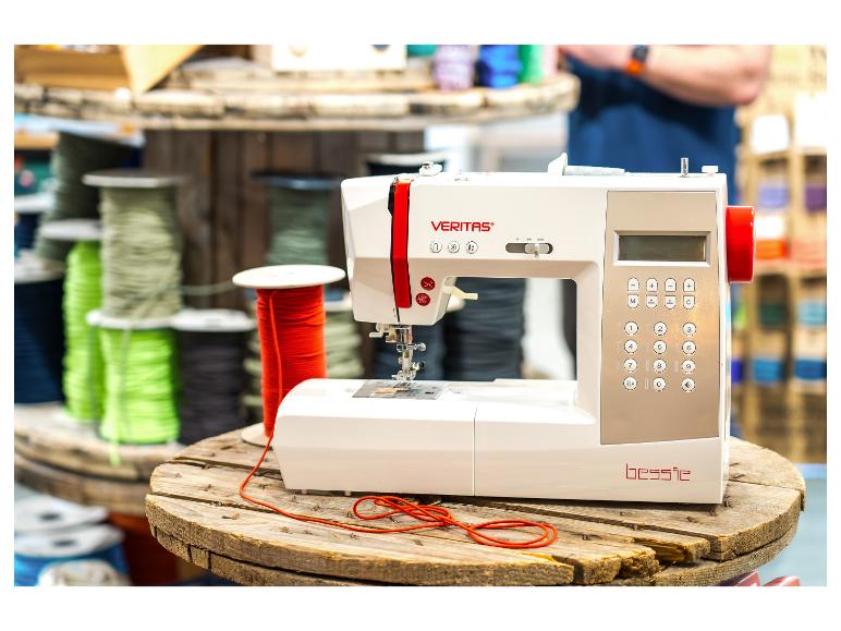 Een witte naaimachine met rode accenten op een houten spoel, omringd door kleurrijke garenspoelen.