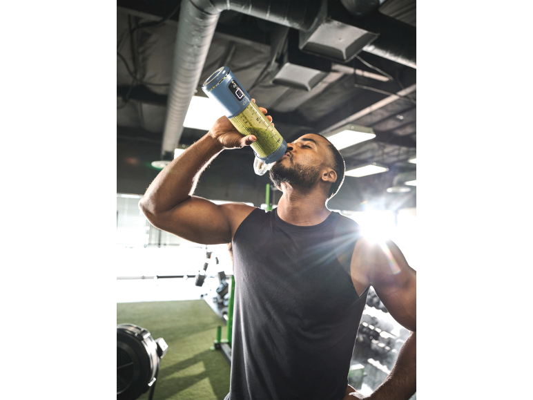 Man drinkt groene smoothie uit draagbare blender in sportschool.