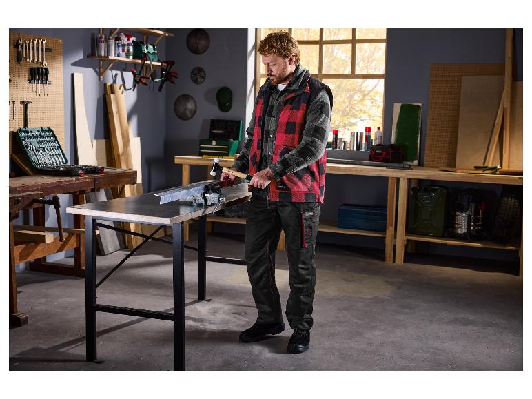 Een man in een werkplaats gebruikt een hamer op een metalen stuk dat in een bankschroef op een werkbank is geklemd.