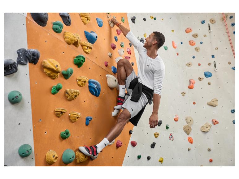 Man in wit shirt met lange mouwen en grijze korte broek aan het boulderen