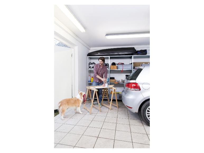 Man schildert hout in garage met hond, naast auto en planken.