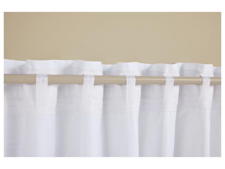 Witte lussen gordijnen aan een lichtbruine gordijnroede tegen een beige muur.