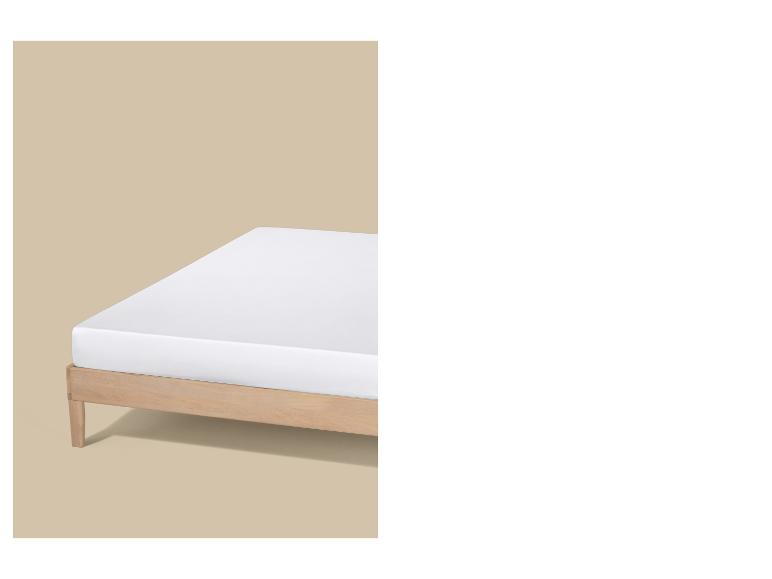 Een wit matras op een licht houten bedframe tegen een beige achtergrond.