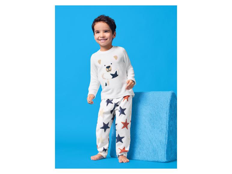 Blije jongen in witte pyjama met beermotief en sterrenprint.