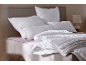 Bed met witte kussens en dekbed met patroon, op een roze laken.
