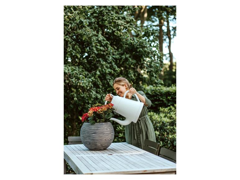 Vrouw giet bloemen in een pot op een houten tuintafel.