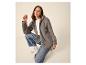 Vrouw in grijs fleecejack, wit T-shirt en blauwe jeans, gehurkt op een lichte achtergrond.