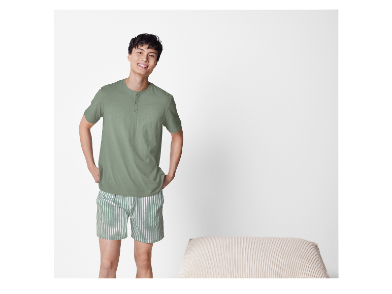 Lachende man in lichtgroene pyjama met korte mouwen en gestreepte shorts.