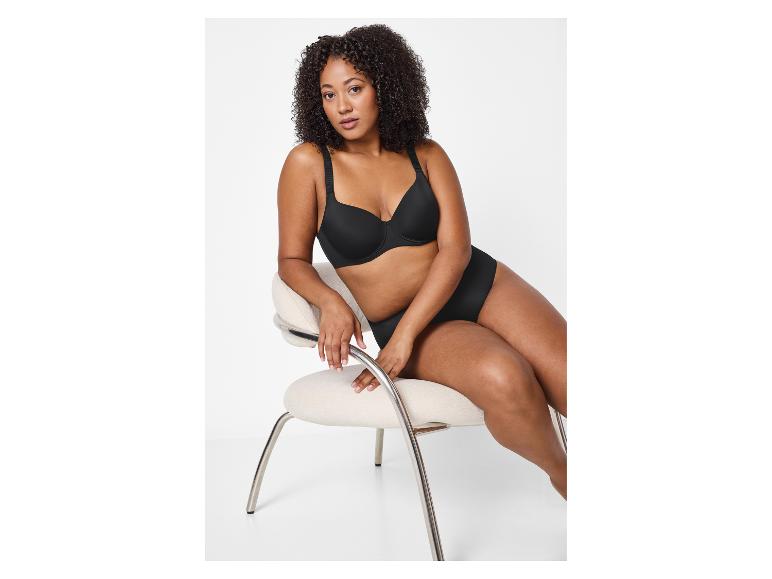 Vrouw zit op stoel in zwarte beha en slip.