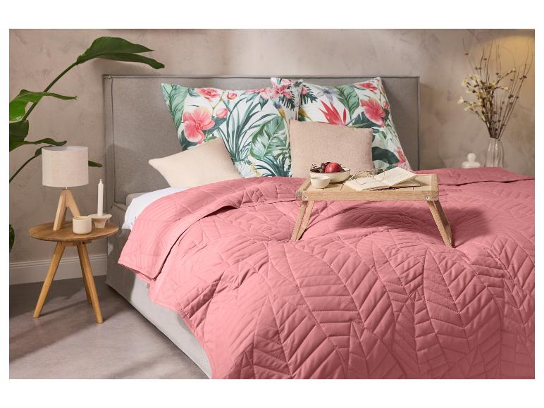 Slaapkamer met een roze sprei, kussens met bloemenpatroon en een houten ontbijtblad.
