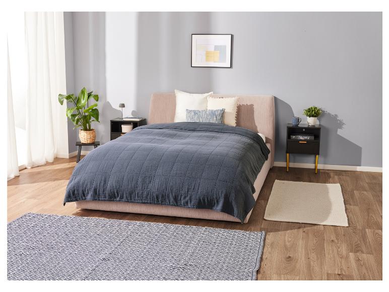 Bed, donkerblauwe deken en nachtkastjes in een moderne slaapkamer.