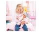 Lachend meisje voedt babypop met fles, omringd door roze slaapkamerdecoratie.