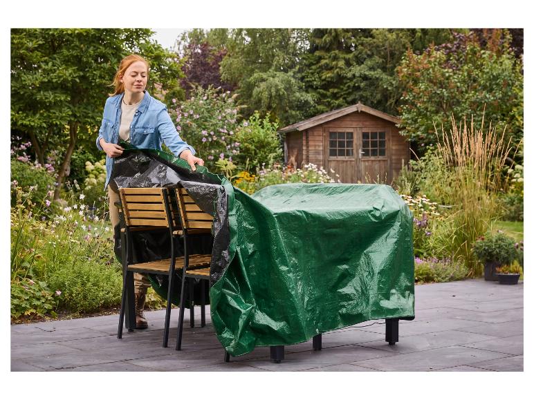 Een vrouw dekt tuinmeubelen af met een groen PARKSIDE universeel afdekzeil.