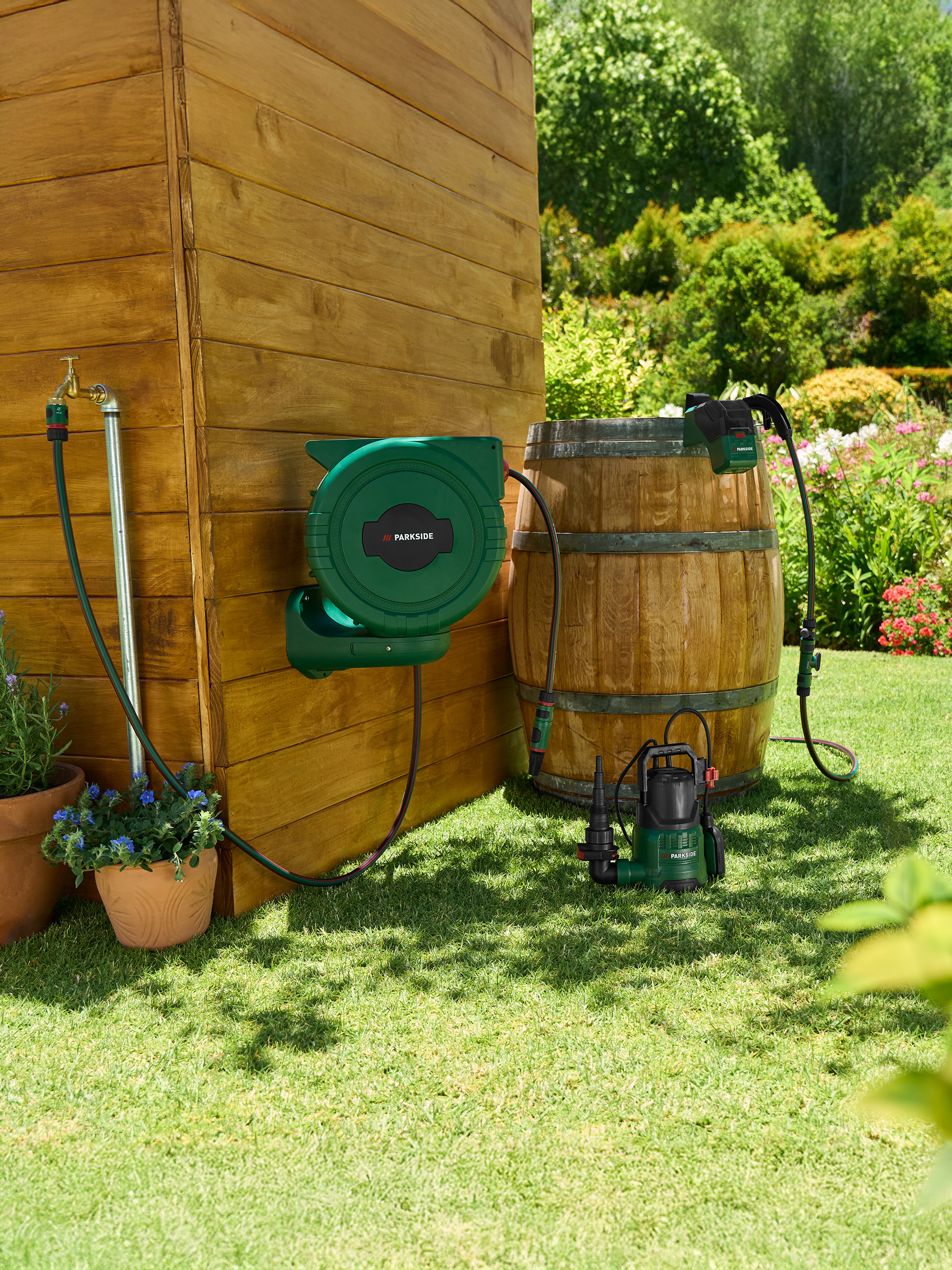 Tuinslanghaspel en pomp bij een houten schuur en vat in de tuin.