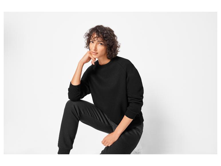 Een vrouw draagt ​​een zwarte trui en broek.