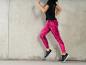 Een vrouw draagt roze sportleggingen en zwarte sneakers.