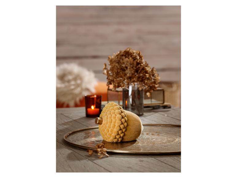 Een decoratief eikelvormig voorwerp van geel fluweel op een metalen dienblad.