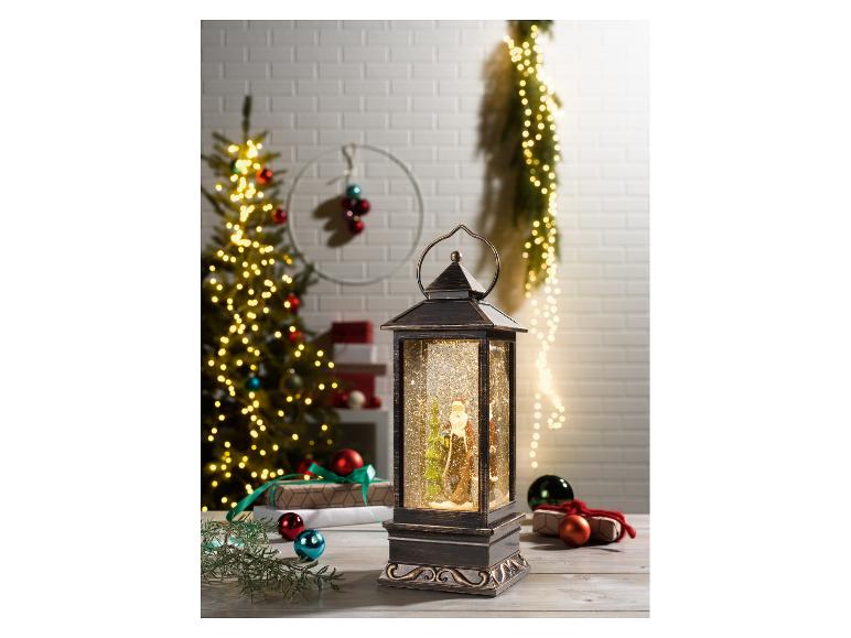 Kerstlantaarn met kerstman en glinsterende sneeuw, omringd door kerstboom en cadeaus.