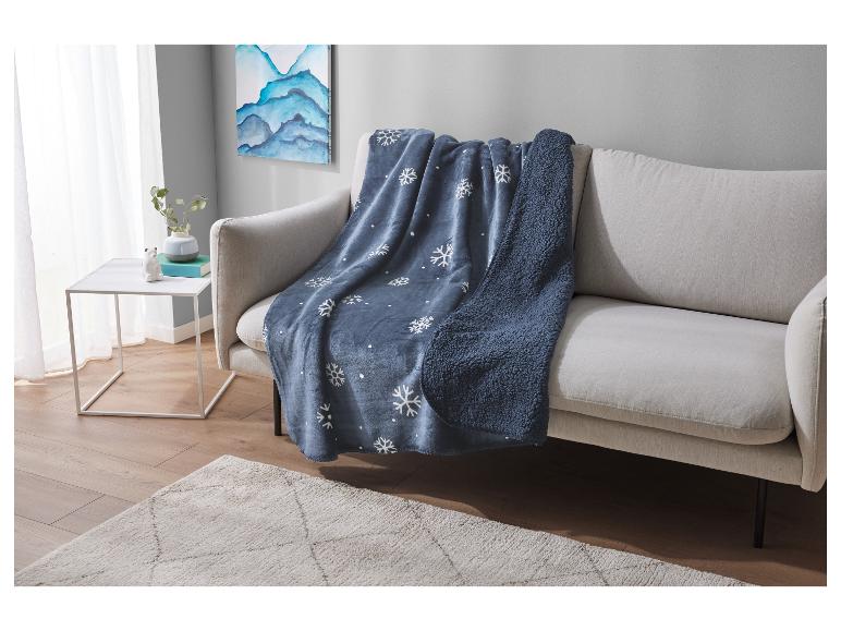 Blauwe deken met sneeuwvlokken op een beige bank in een moderne woonkamer.