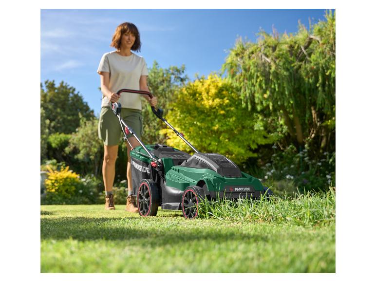 Een vrouw maait een zonnig gazon met een groene en zwarte grasmaaier.