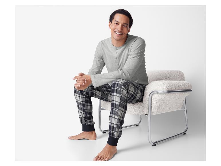 Lachende man in geruite pyjama, zittend op een witte fauteuil.