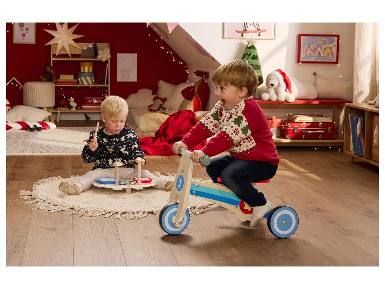 Twee jonge jongens spelen met een houten loopfiets en een drumstel in een feestelijke kamer.