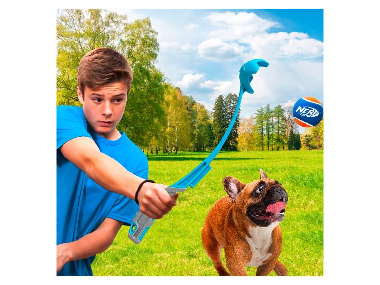 Jongen speelt apporteren met een hond met een ballenwerper in een park.