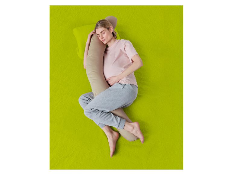 Vrouw slaapt op haar zij met een lichaamskussen op een groene achtergrond.