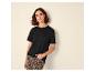 Vrouw in zwart T-shirt en luipaardprint broek, leunend tegen een muur.