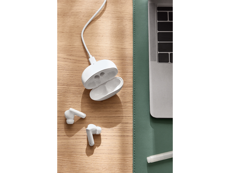 Witte draadloze oordopjes met oplaadcase op een houten bureau naast een laptop