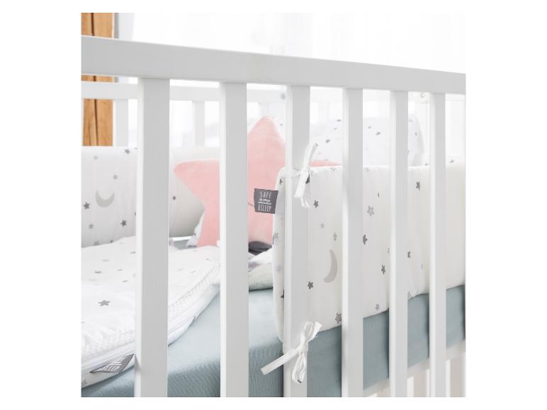 Babybedje met wit beddengoed met sterren en maan, en een roze kussen.