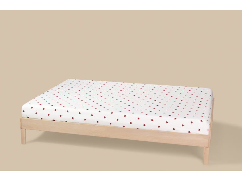 Wit hoeslaken met rode hartjes op een houten bed.