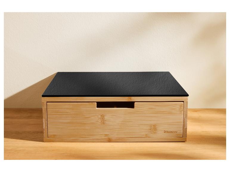 Een houten broodtrommel met een zwart leisteenachtig deksel op een houten ondergrond.