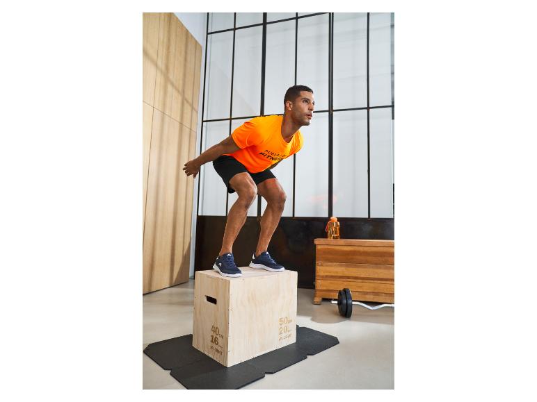 Man in oranje t-shirt en zwarte korte broek traint met een houten kist.