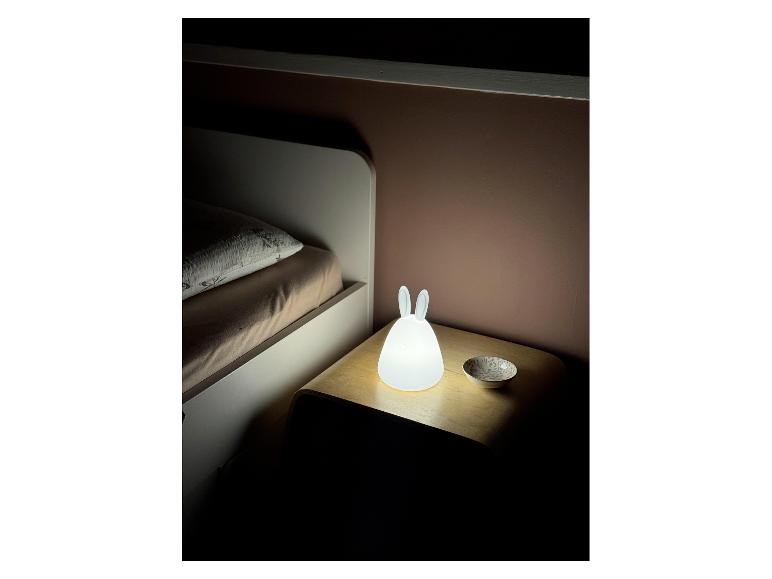 Nachtlampje in de vorm van een konijn op een nachtkastje naast een bed.