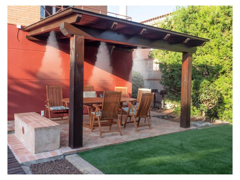 Tuinset met houten tafel en stoelen onder een pergola met watervernevelaar.