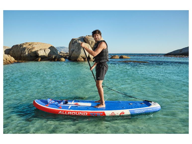 Man op blauw en rood opblaasbaar paddleboard in helder water, met rotsen op de achtergrond.