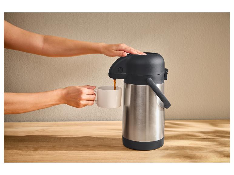 Een persoon schenkt koffie uit een zilveren thermoskan in een witte mok.
