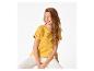 Vrouw in gele geborduurde blouse en witte broek, zittend op een stoel.