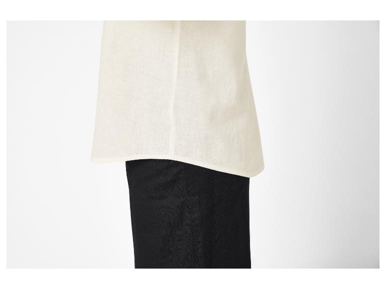 Close-up van een persoon die een crèmekleurige linnen top over een zwarte broek draagt.