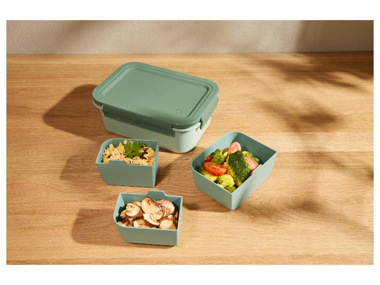 Lunchbox en drie kleinere voedselcontainers op een houten tafel.
