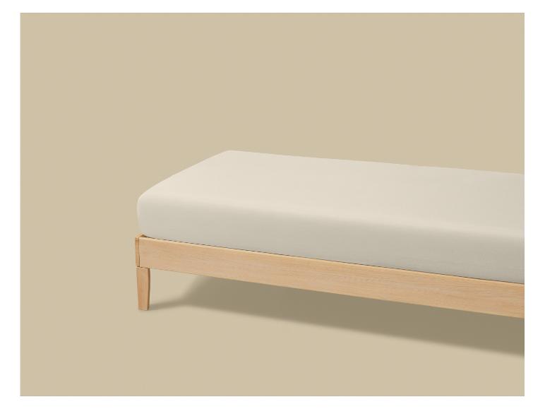Houten bed met crèmekleurig matras op een beige achtergrond.