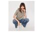 Vrouw in een kaki T-shirt, wijde jeans en witte sneakers, lachend.