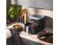 Zwarte airfryer op een aanrecht naast gebakken aardappelen en sauzen.