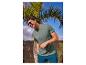 Man in groen T-shirt met 'Thrive in the unknown' tekst, blauwe korte broek en zonnebril.