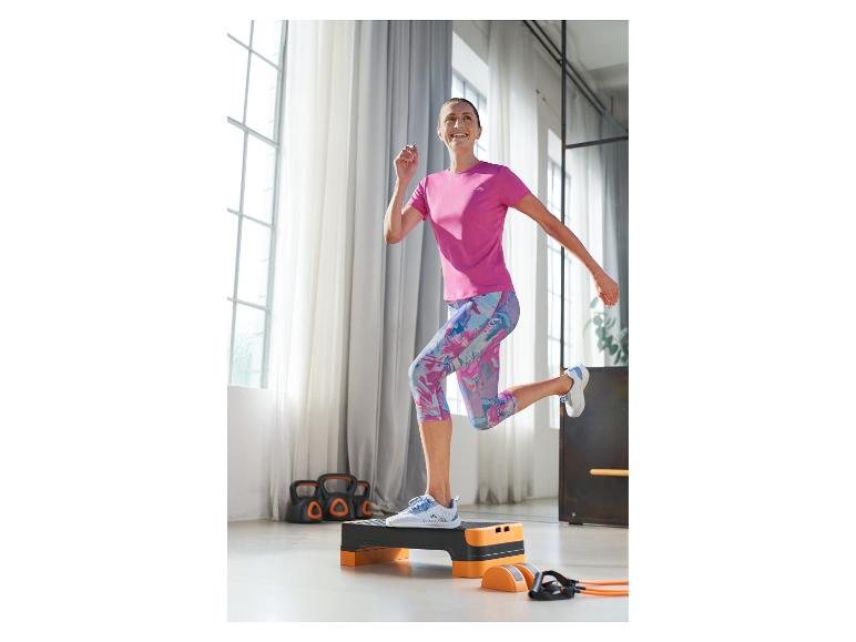Vrouw in roze sportshirt en zwart-oranje stepbank aan het trainen