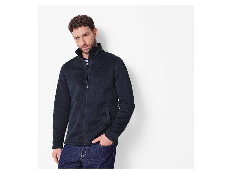 Man in een marineblauwe fleecejas en blauwe jeans.